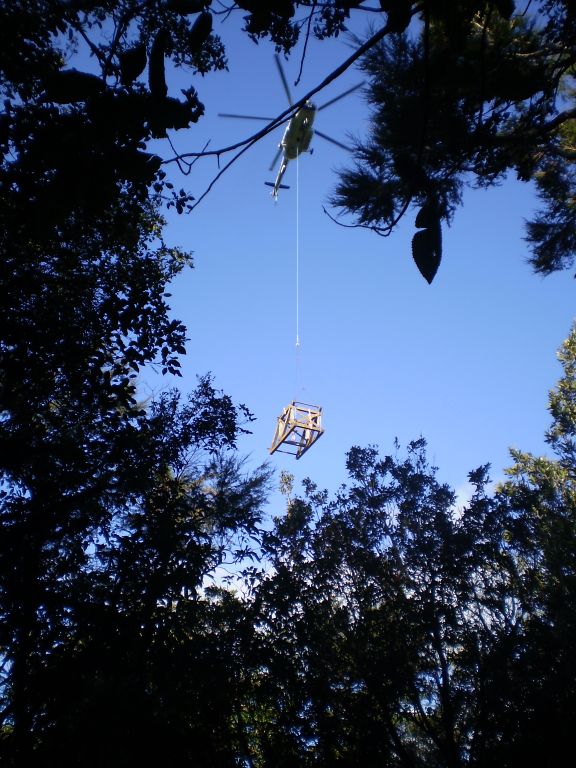 The helicopter carefully lowers the headframe through an opening in the forest